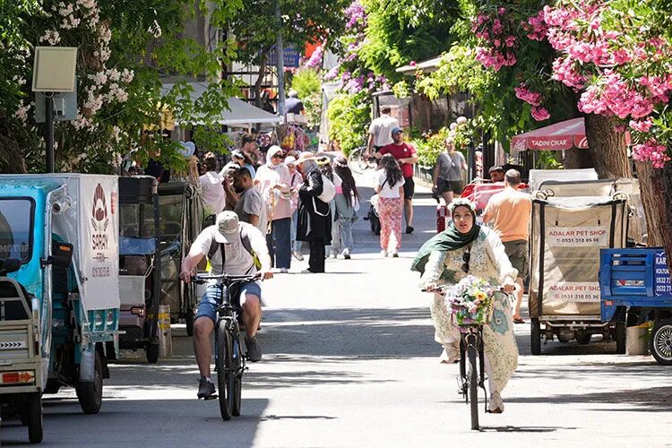 Car-free street on Büyükada with visitors cycling past flowering trees
